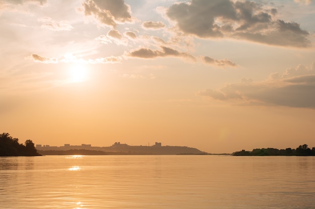 Ruhige Wasseroberfläche mit gelbem Sonnenuntergangshimmel und Sonne durch die Wolken über Meditationswasser und -himmel