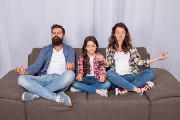 Ruhige Yoga-Meditation Familientag Freundschaft Vater Mutter und Kind auf dem Sofa freundliche Familie, die Spaß hat glückliche Eltern mit Kind Mädchen zu Hause Mama Papa und Tochter lieben es, sich zusammen zu entspannen