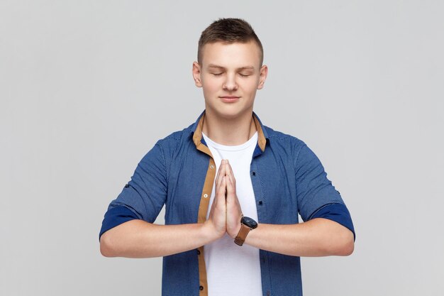 Foto ruhiger, attraktiver teenager-junge, der in yoga-pose steht und versucht, sich zu entspannen, hält die handflächen zusammen