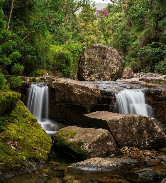 Foto ruhiger doppelter wasserfall, der auf einem felsigen fluss inmitten des dschungels absteigt