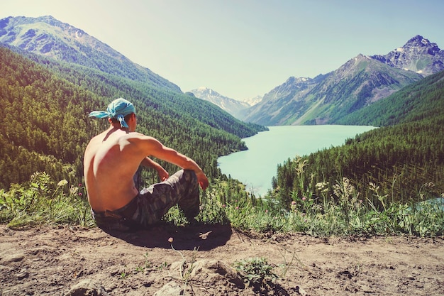 Ruhiger mann, der im urlaub auf einem felsen sitzt und an einem sommerabend auf den see und die berge blickt bergsee kucherlinskoe von oben altay russland