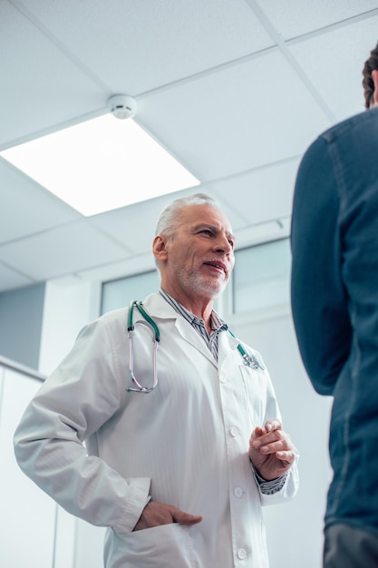 Ruhiger reifer Arzt, der in der Nähe des Patienten steht und ein ruhiges Gespräch führt stockfoto