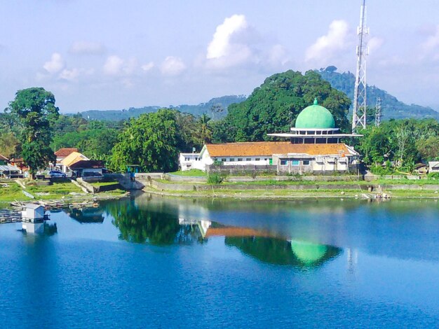 Foto ruhiger see, umgeben von üppig grünen bäumen mit einem weißen gebäude mit einer moschee im hintergrund