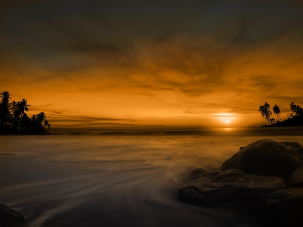 Ruhiger Strand bei Sonnenuntergang mit Felsen