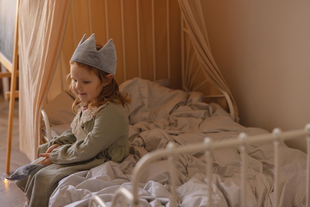 Ruhiges hellhäutiges kleines rothaariges Mädchen im Kleid nach Spielen sitzt auf dem Bett vor dem Mittagsschlaf zu Hause Kinderkonzept