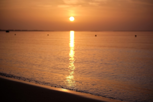 Ruhiges Meer mit Wellen am Sandstrand bei Sonnenaufgang.