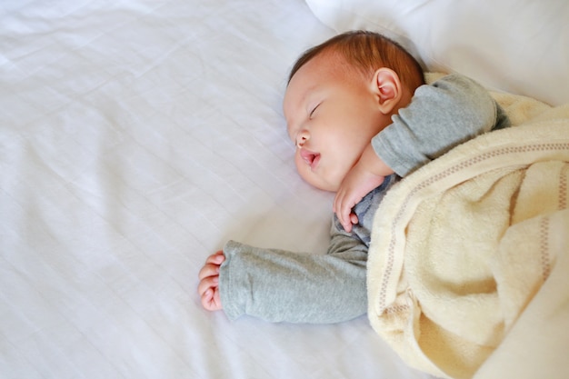 Ruhiges neugeborenes asiatisches Baby, das auf Bett mit der Decke schläft.