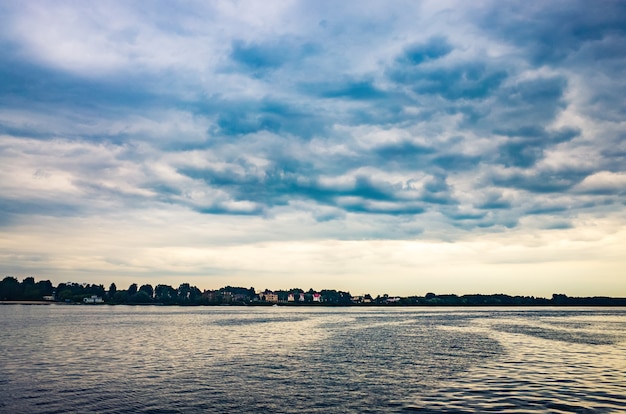 Ruhiges Wasser und schöner blauer Himmel mit Wolken Bäume wachsen am nächsten Ufer Textfreiraum