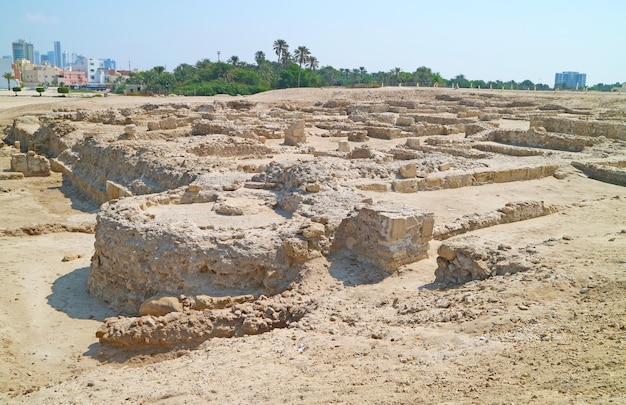 Foto ruinas de la estructura del fuerte de bahrein con el paisaje urbano moderno de manama en el fondo