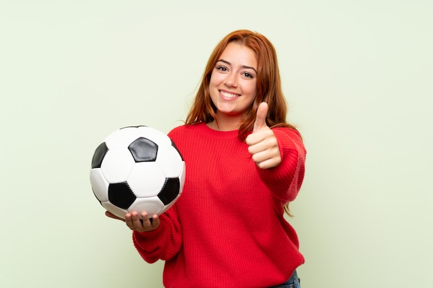 Ruiva adolescente com camisola sobre verde isolado, segurando uma bola de futebol