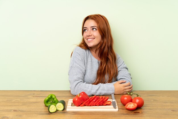 Ruiva adolescente com legumes em uma mesa, rindo e olhando para cima