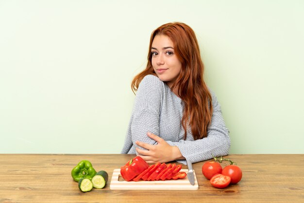 Ruiva adolescente com legumes em uma mesa rindo