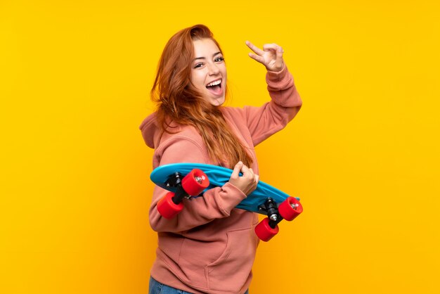 Ruiva adolescente com skate sobre parede amarela isolada