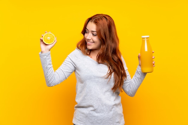 Ruiva adolescente segurando uma laranja sobre amarelo isolado