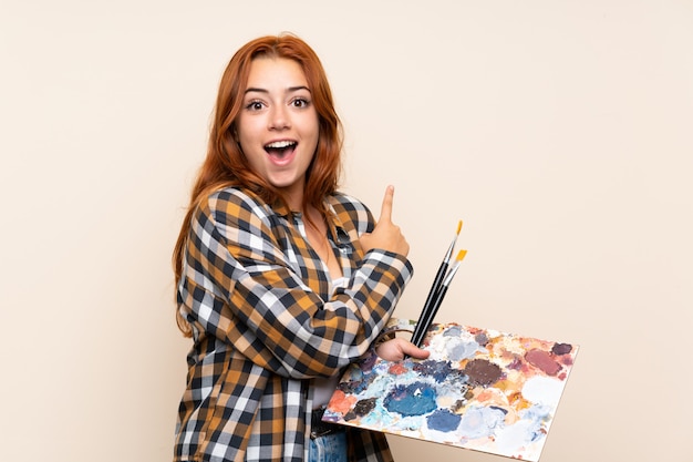 Ruiva adolescente segurando uma paleta sobre dedo apontando isolado para o lado