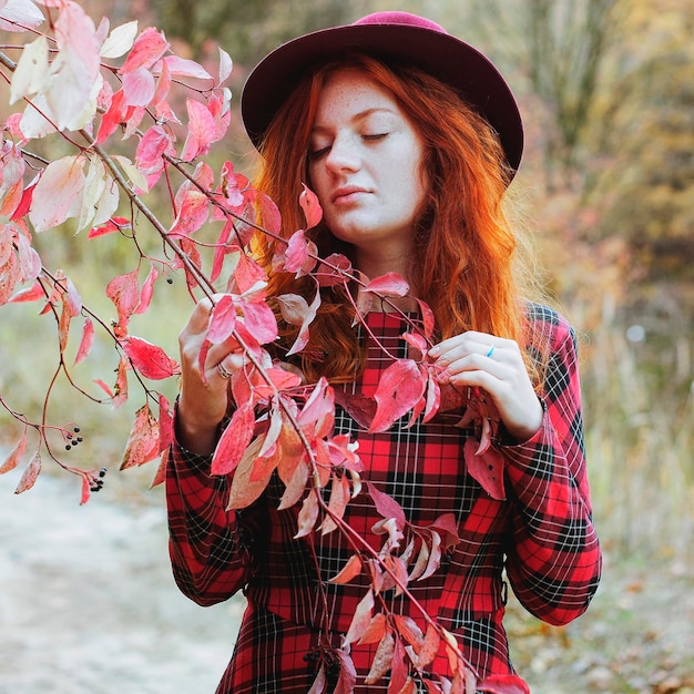 Ruiva de vestido vermelho, chapéu andando na floresta de outono. estilo de vida feliz. outono. folhas amarelas