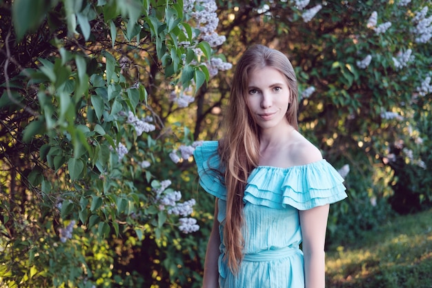 Ruiva em vestido de cocktail azul claro em arbustos lilás