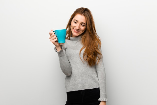 Ruiva na parede branca, segurando uma xícara de café quente