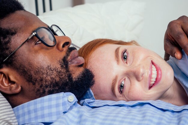 Ruivo ruivo caucasiano feliz feminino e multiétnico homem afro juntos deitado na cama bedroom.lifestyle tolerância conceito.