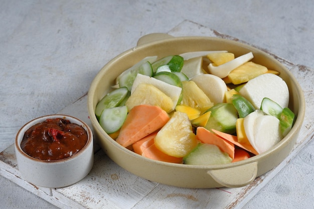 rujak buah oder indonesischer obstsalat auf weißem teller serviert mit süßer würziger sauce und gemahlener erdnuss