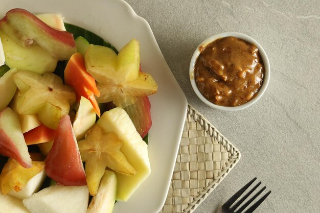 Rujak Buah oder traditioneller indonesischer Obstsalat auf grauem Teller, serviert mit würziger brauner Zuckersauce