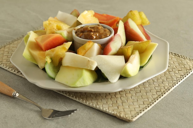 Foto rujak buah ou salada de frutas tradicional indonésia em prato cinza servido com molho picante de açúcar mascavo