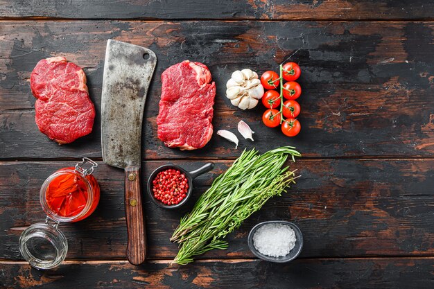 Rumpsteak corte de carne orgánica, filete de ternera cruda marmolada, con cuchillo de carnicero y condimentos en la mesa rústica de madera oscura, vista superior.