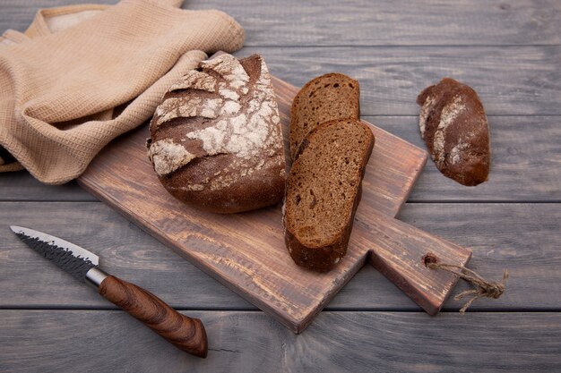 Rundbrot aus Roggenbrot, mit einem Messer aus rustikalem Holz auf einem Holzbrett in Stücke geschnitten. Draufsicht.