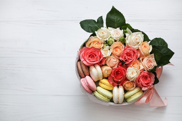 Runde Box mit Rosen und Kuchenmakronen auf Hintergrund Blumen in voller Blüte Geschenkblumen-Komposition