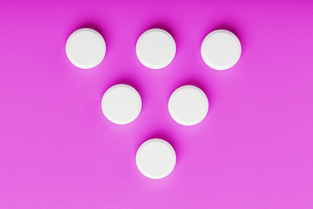 Runde Ecstasy-Tabletten in Form eines Dreiecks auf einer rosa Oberfläche