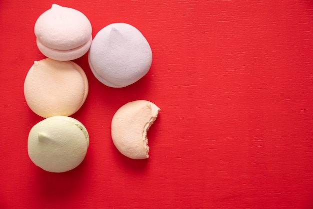 Runde, mehrfarbige Marshmallows in einem Stapel und eine gebissene Hälfte eines Marshmallows auf rotem Hintergrund, Kopierraum von oben. Köstliche Süßigkeiten und Lebensmittelhintergrund.