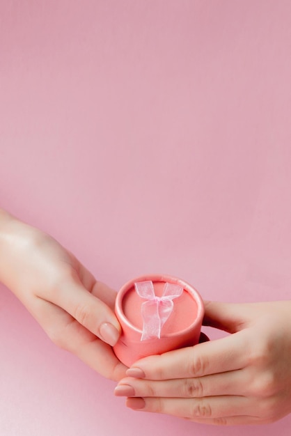 Foto runde rosa geschenkkiste in frauenhänden auf rosa hintergrund feierliches konzept für valentinstag, muttertag oder geburtstag