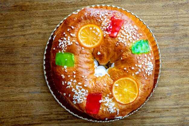 Runde Weihnachtsfruchtkuchen verziert mit Tannenzweig, glasierten Früchten und Nüssen auf einem Holztisch.