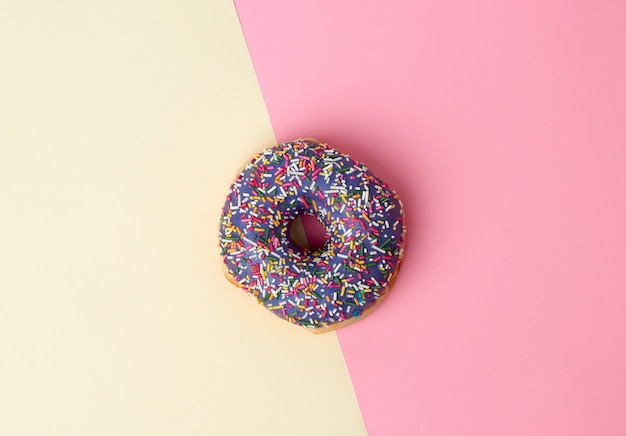 Runder gebackener Donut mit farbigem Zucker besprüht auf einem rosa-gelben Hintergrund