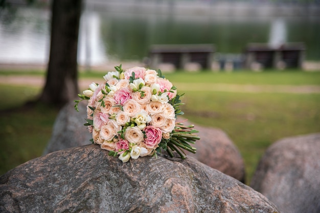 Runder Hochzeitsstrauß aus weißen, rosa und gelben Rosen liegt auf der Steinnahaufnahme