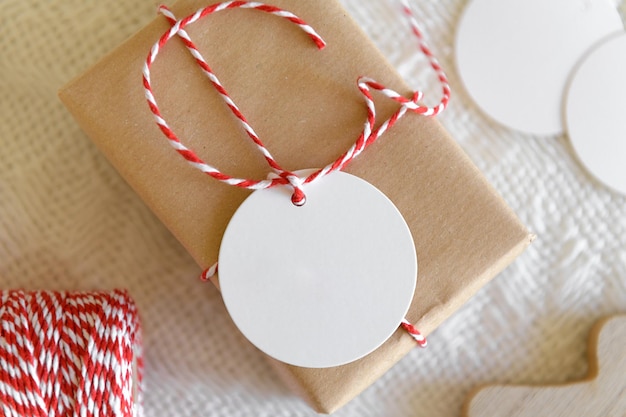 Rundes leeres Geschenkanhänger-Mockup auf Geschenk-Kraft-Box Weihnachten einfaches Blankopapier-Etiketten-Mockup mit Schnur auf Geschenkbox auf gestricktem beigem Hintergrund