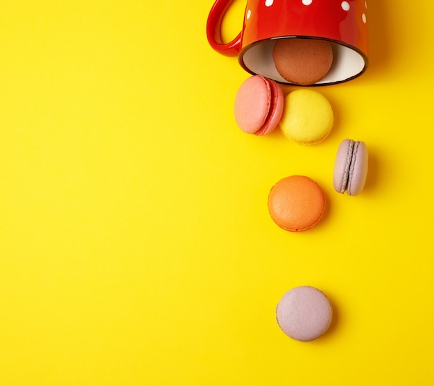 Rundes mehrfarbiges macarons, das von einer roten keramischen Schale fällt