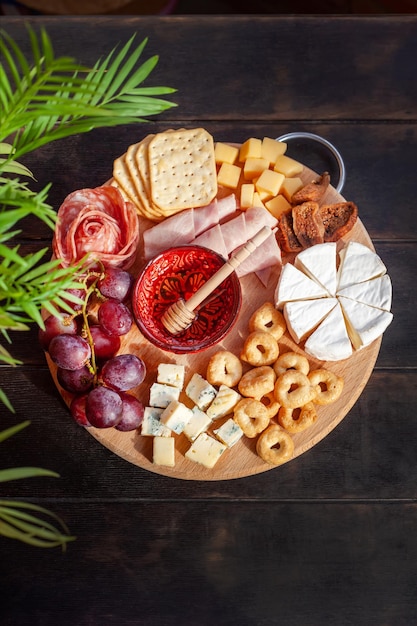 Rundes Schneidebrett mit in Scheiben geschnittener Käse Wurst Rosette Schinken Cracker Trauben und Feigen mit Honig Charcuterie und Käseplatte Draufsicht