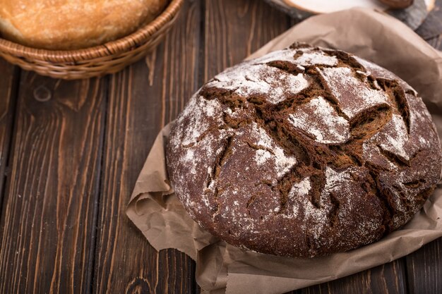 Rundes warmes frisches Schwarzbrot auf altem Holztisch mit Serviette, horizontal