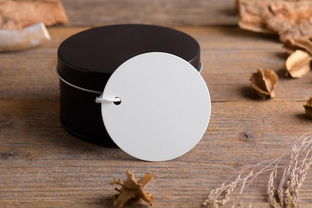 Rundes weißes Geschenkanhängermodell auf schwarzer runder Schachtel auf rustikalem Holzhintergrund mit Boho-Dekoration
