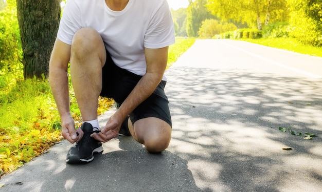 Foto runner atarse los cordones de los zapatos para correr en el parque de verano se está preparando para el entrenamiento de jogging