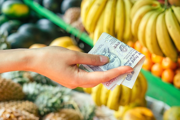 Rúpias indianas nas mãos de mulheres escolhem frutas no mercado asiático. conceito de turismo e recreação.