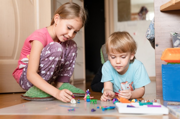 Rusia, Moscú, octubre de 2020 - dos pequeños niños felices, un niño de cuatro años y una niña de siete años, hermanos o amigos en casa en el piso juntos jugando y esculpiendo con plastilina