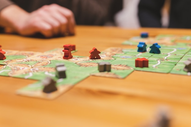 Foto rússia, dezembro de 2020: dois amigos homens se divertem jogando o jogo de tabuleiro carcassonne tarde da noite ou à noite. mãos masculinas e cartas de jogo e fichas na mesa