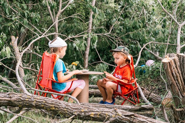 Rússia, julho de 2020 - crianças, um menino e uma menina amigos fazem um piquenique divertido e comem entre as árvores caídas no verão em uma vila no campo nas férias