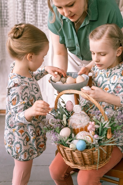 Foto rússia moscou 04092022 feliz feriado de páscoa na primavera temporada família mãe e crianças pequenas meninas decoram uma cesta de vime com ovos e bolos assados decoração festiva para casa comida tradicional