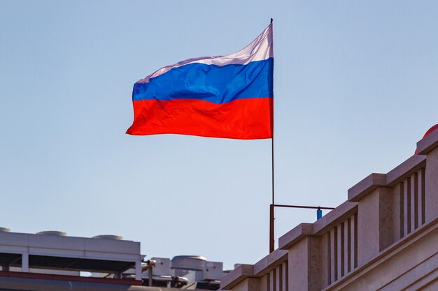 Russische Flagge auf Fahnenmast, der auf dem Wind gegen Gebäudedächer und blauen Himmel weht