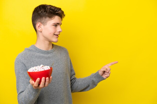 Russische Frau des Teenagers, die einen gelben Hintergrund hält, der auf die Seite zeigt, um ein Produkt zu präsentieren