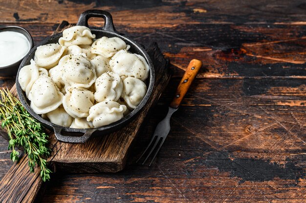 Russische Knödel Pelmeni mit Rind- und Schweinefleisch. Dunkler Holztisch. Draufsicht.