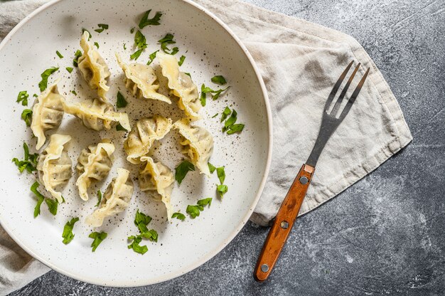 Russische Pelmeni Mehlklöße gefüllt mit Fleisch mit Butter und Gemüse. Grauer Hintergrund. Ansicht von oben